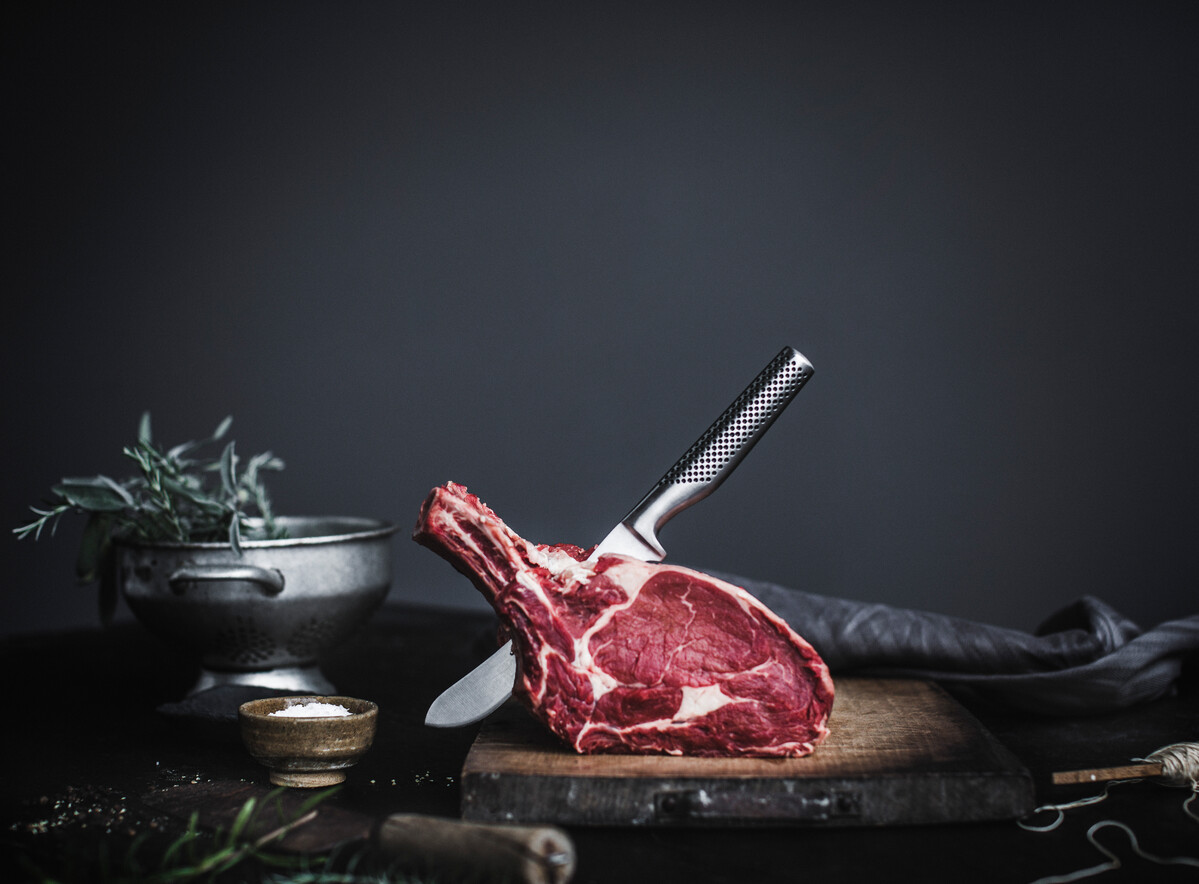 Een Global slagersmes in een côte de boeuf op een donkere tafel